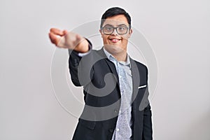 Young hispanic man with down syndrome wearing business style smiling friendly offering handshake as greeting and welcoming