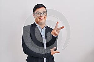 Young hispanic man with down syndrome wearing business style smiling with happy face winking at the camera doing victory sign