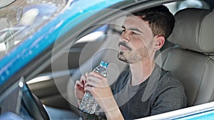 Young hispanic man drinking bottle of water driving car at street