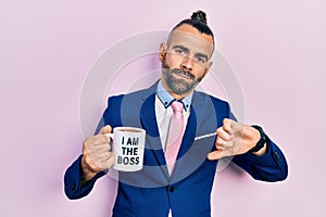 Young hispanic man drinking from i am the boss coffee cup with angry face, negative sign showing dislike with thumbs down,