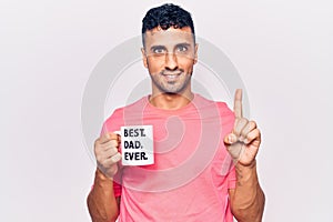 Young hispanic man drinking mug of coffe with best dad ever message smiling with an idea or question pointing finger with happy