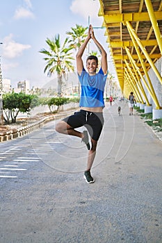 Young hispanic man exercising doing tree pose outdoors