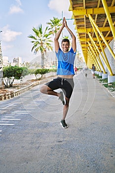 Young hispanic man exercising doing tree pose outdoors