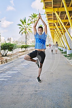 Young hispanic man exercising doing tree pose outdoors