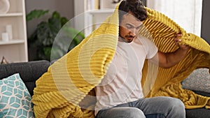 Young hispanic man feeling cold covered with blanket at home