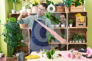 Young hispanic man florist holding gift lace at flower shop