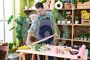 Young hispanic man florist holding gift lace at flower shop