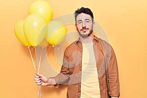 Young hispanic man holding balloons thinking attitude and sober expression looking self confident