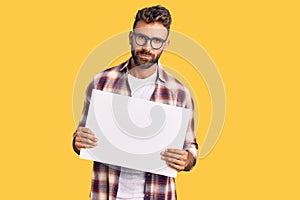 Young hispanic man holding blank empty banner thinking attitude and sober expression looking self confident