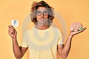 Young hispanic man holding brain and question mark looking at the camera blowing a kiss being lovely and sexy