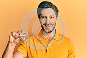 Young hispanic man holding brilliant diamond stone looking positive and happy standing and smiling with a confident smile showing