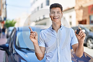 Young hispanic man holding car key smiling happy pointing with hand and finger to the side