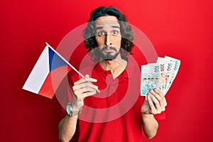 Young hispanic man holding czech republic flag and koruna banknotes depressed and worry for distress, crying angry and afraid