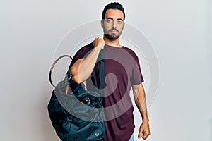 Young hispanic man holding gym bag thinking attitude and sober expression looking self confident