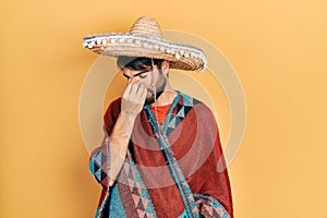 Young hispanic man holding mexican hat tired rubbing nose and eyes feeling fatigue and headache