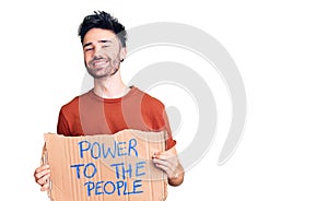 Young hispanic man holding power to the people banner looking positive and happy standing and smiling with a confident smile