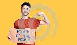 Young hispanic man holding power to the people banner pointing finger to one self smiling happy and proud