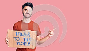 Young hispanic man holding power to the people banner smiling happy pointing with hand and finger to the side