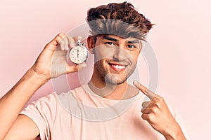 Young hispanic man holding stopwatch smiling happy pointing with hand and finger
