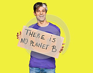 Young hispanic man holding there is no planet b banner looking positive and happy standing and smiling with a confident smile