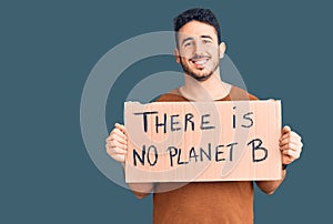 Young hispanic man holding there is no planet b banner looking positive and happy standing and smiling with a confident smile