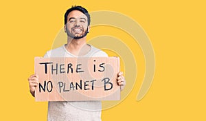 Young hispanic man holding there is no planet b banner looking positive and happy standing and smiling with a confident smile