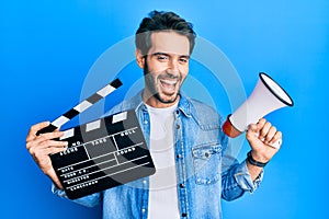 Young hispanic man holding video film clapboard and megaphone smiling and laughing hard out loud because funny crazy joke