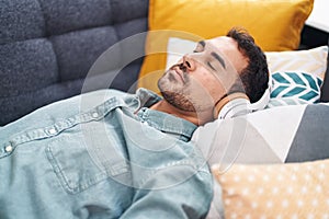 Young hispanic man listening to music sleeping on sofa at home