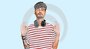 Young hispanic man listening to music using headphones relax and smiling with eyes closed doing meditation gesture with fingers