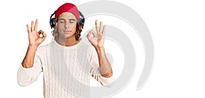 Young hispanic man listening to music using headphones relax and smiling with eyes closed doing meditation gesture with fingers