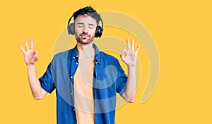 Young hispanic man listening to music using headphones relax and smiling with eyes closed doing meditation gesture with fingers