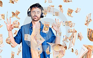 Young hispanic man listening to music using headphones relax and smiling with eyes closed doing meditation gesture with fingers