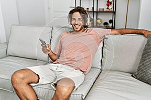 Young hispanic man listening to music using smartphone at home