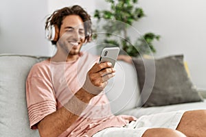 Young hispanic man listening to music using smartphone at home