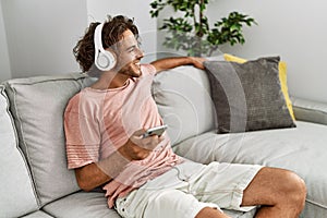 Young hispanic man listening to music using smartphone at home