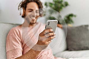 Young hispanic man listening to music using smartphone at home