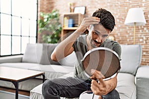 Young hispanic man lookin hair on mirror at home