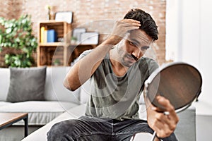 Young hispanic man lookin hair on mirror at home