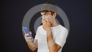 Young hispanic man looking at smartphone with surprise expression over isolated black background