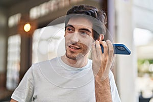 Young hispanic man miling confident listening audio message by the smartphone at street