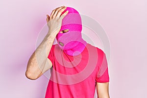 Young hispanic man with modern dyed hair wearing pink balaclava mask face surprised with hand on head for mistake, remember error