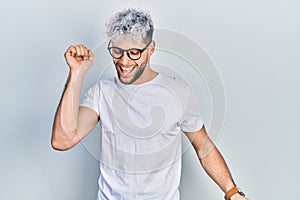 Young hispanic man with modern dyed hair wearing white t shirt and glasses dancing happy and cheerful, smiling moving casual and