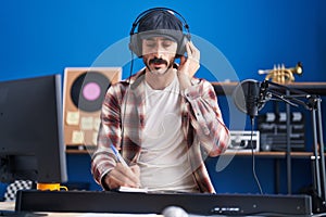 Young hispanic man musician listening to music composing song at music studio