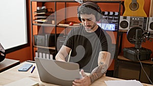 Young hispanic man musician using laptop and headphones at music studio