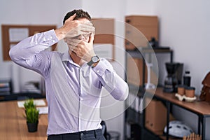 Young hispanic man at the office covering eyes and mouth with hands, surprised and shocked