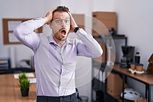 Young hispanic man at the office crazy and scared with hands on head, afraid and surprised of shock with open mouth