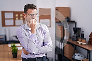 Young hispanic man at the office looking stressed and nervous with hands on mouth biting nails