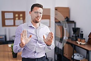 Young hispanic man at the office moving away hands palms showing refusal and denial with afraid and disgusting expression
