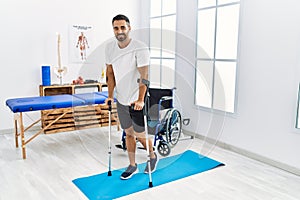 Young hispanic man patient having rehab session walking using crutches at clinic