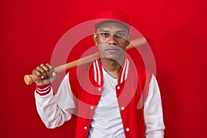 Young hispanic man playing baseball holding bat relaxed with serious expression on face